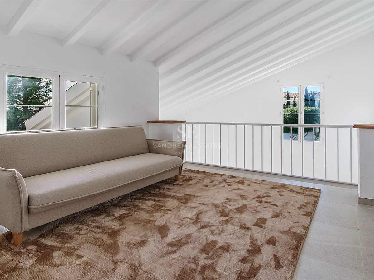 Salon en mezzanine avec canapé beige, tapis brun texturé et plafond mansardé avec poutres en bois blanc.