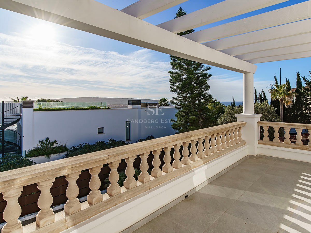 Grande terrasse avec balustrade en pierre et pergola blanche offrant une vue sur le paysage côtier.