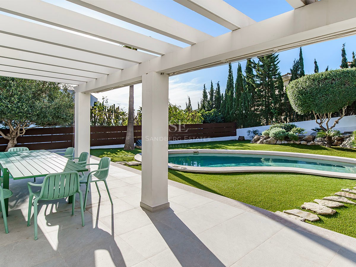Terrasse ombragée avec coin repas vert donnant sur une piscine de forme libre et un jardin paysager avec cyprès.