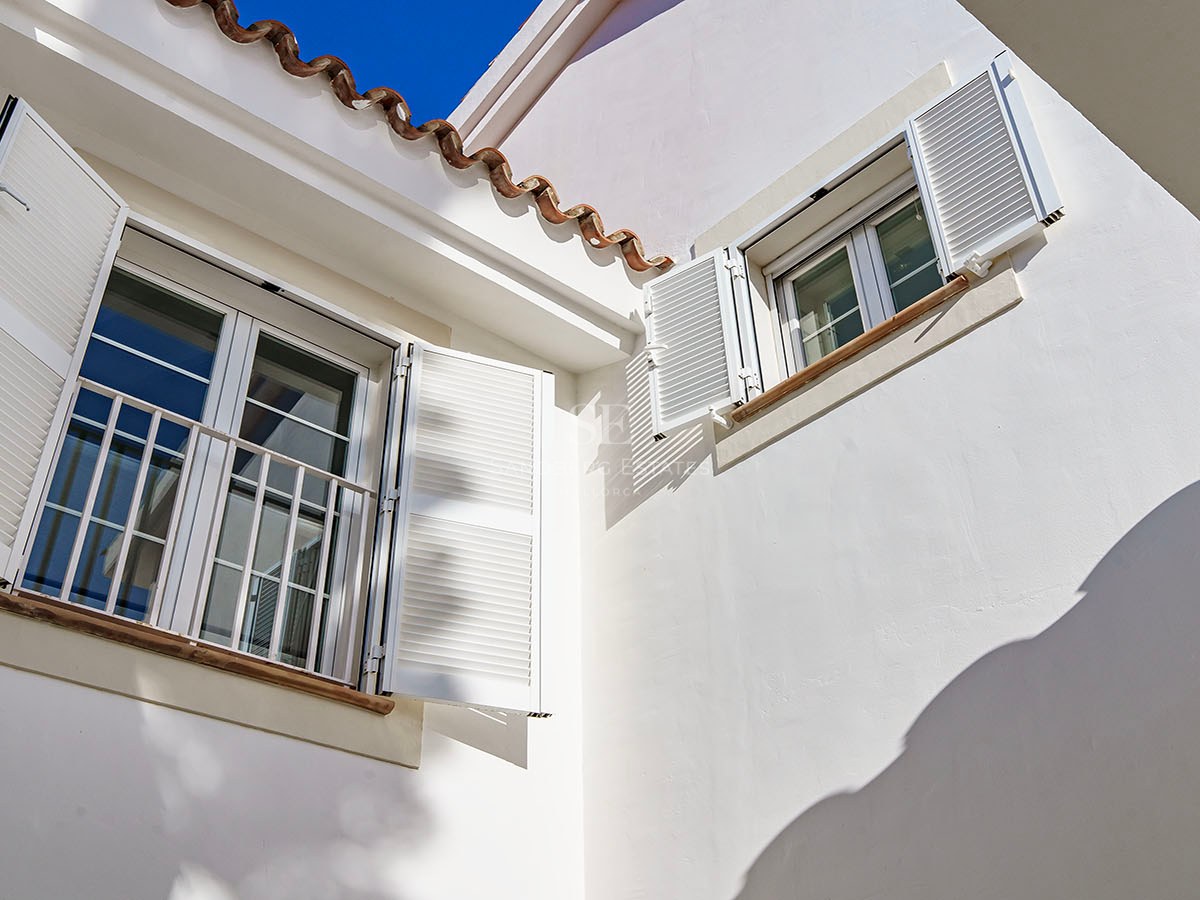 Détail d'une façade blanche avec volets majorquins, tuiles en terre cuite et appuis de fenêtre en pierre.