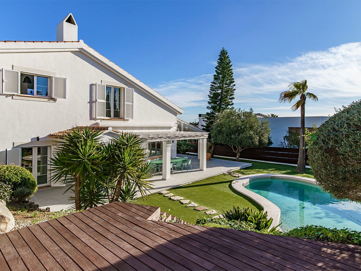 Villa blanche à deux étages avec une piscine en forme de haricot, une terrasse en bois et un jardin arboré.