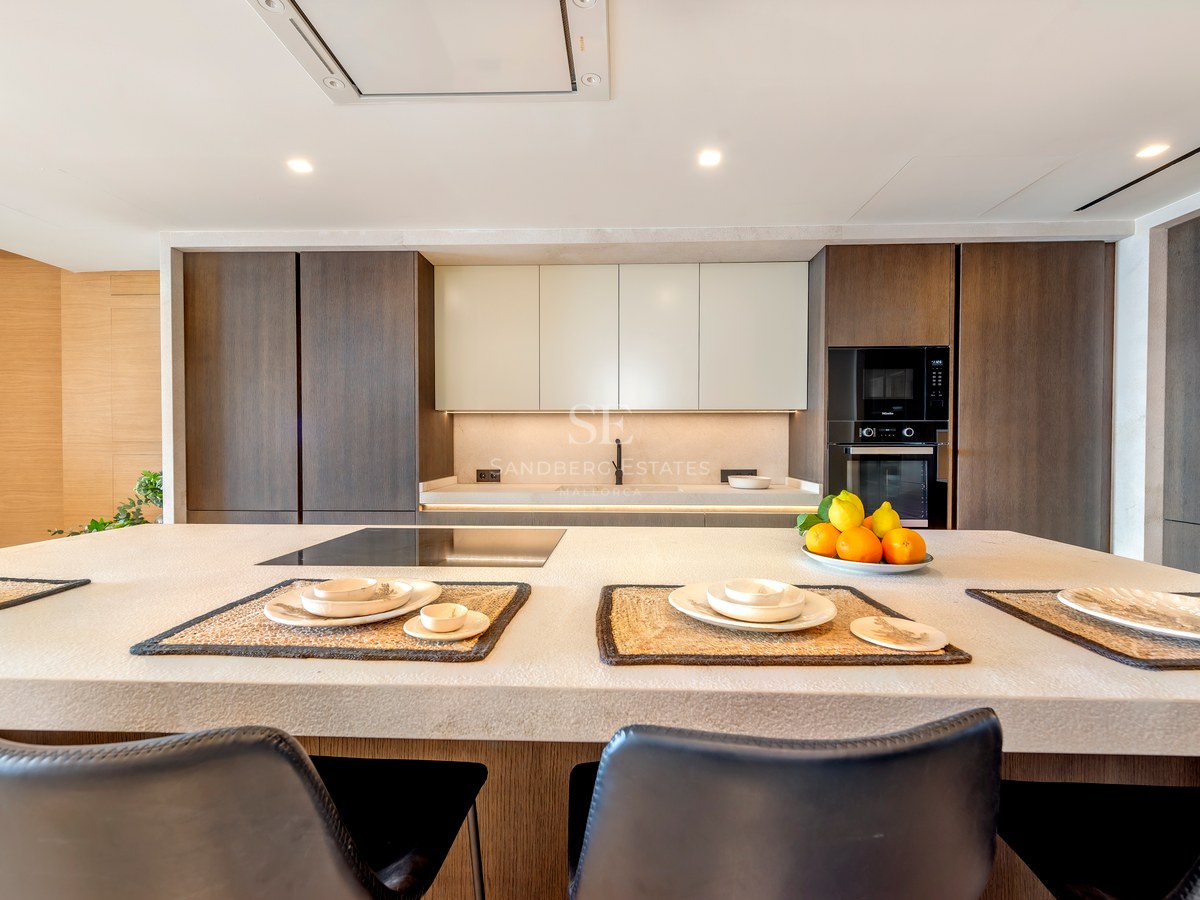 Cocina moderna con una gran isla de piedra texturizada, armarios de madera oscura y electrodomésticos integrados.