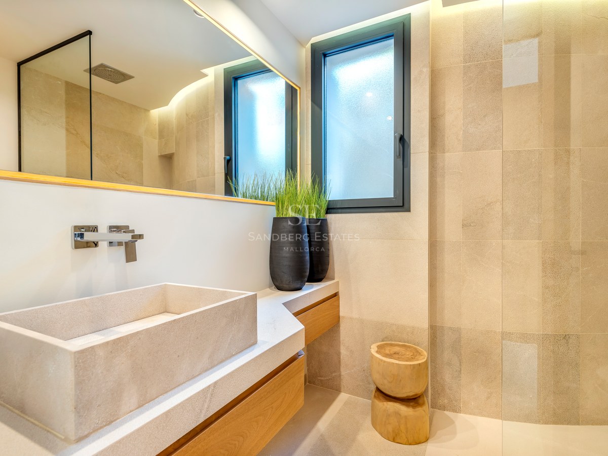 Baño contemporáneo con lavabo de piedra sobre mueble de madera, azulejos de piedra natural e iluminación suave.