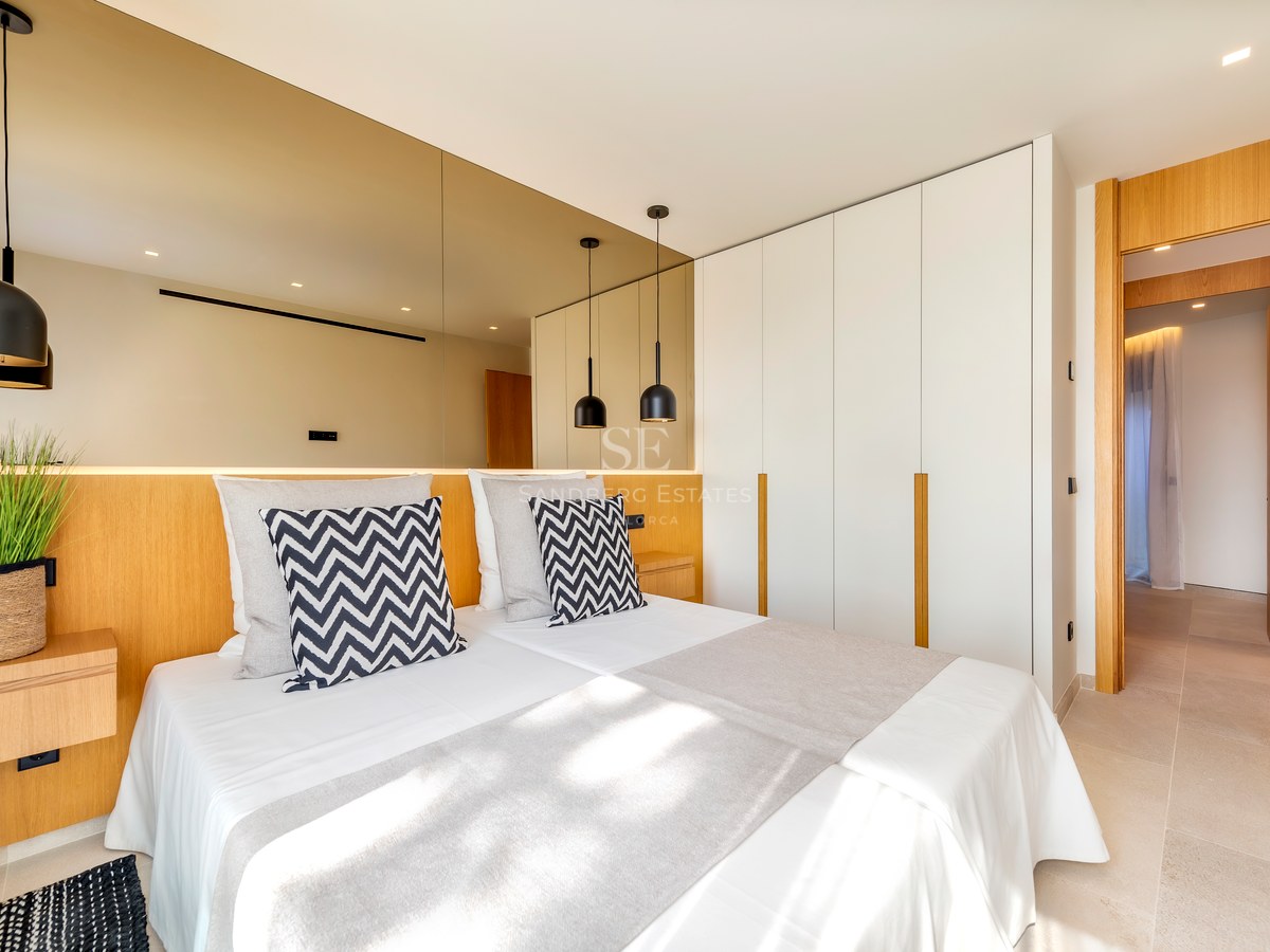Dormitorio contemporáneo con cabecero de madera integrado, pared de espejos y armarios empotrados blancos.