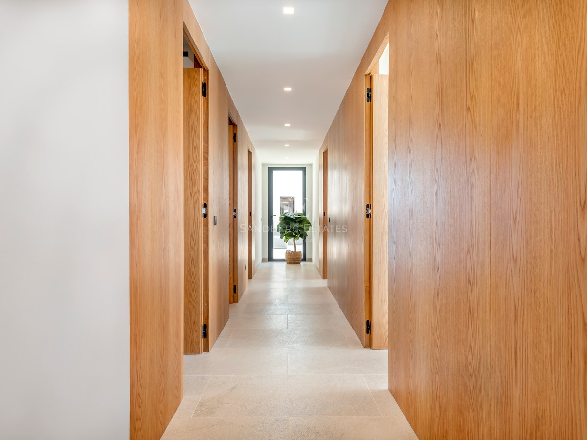 Pasillo moderno con paneles de madera de roble de suelo a techo y puertas integradas bajo una iluminación cálida.