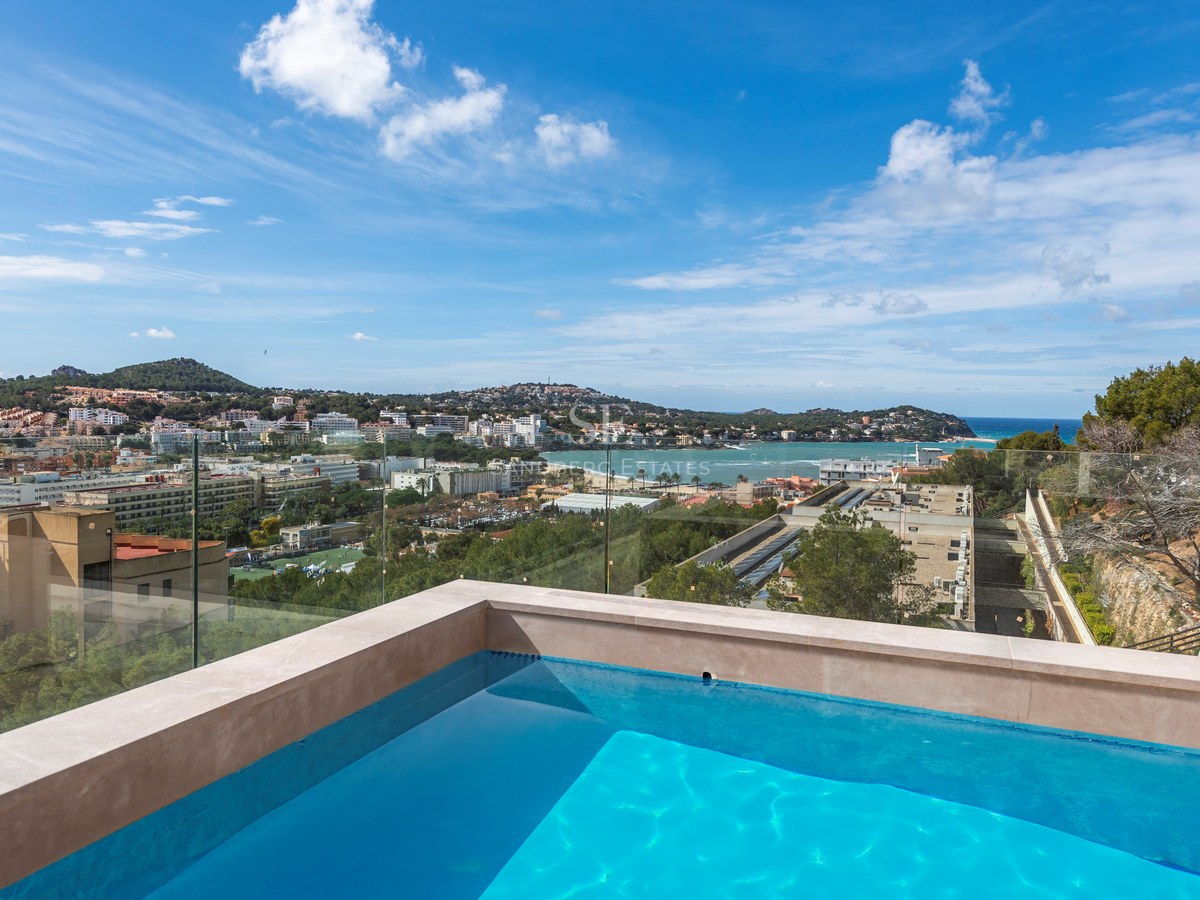 Piscina en la azotea con barandillas de cristal con vistas a un pueblo costero mediterráneo y al mar.