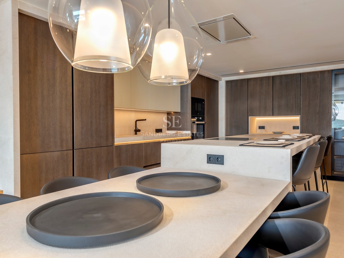 Cocina moderna con armarios de madera oscura, isla de piedra clara con taburetes y lámparas colgantes de cristal.