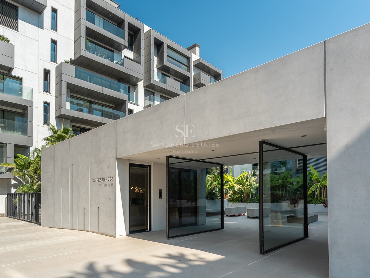 Architectural concrete entrance with oversized glass pivot doors leading into a luxury modern apartment complex.