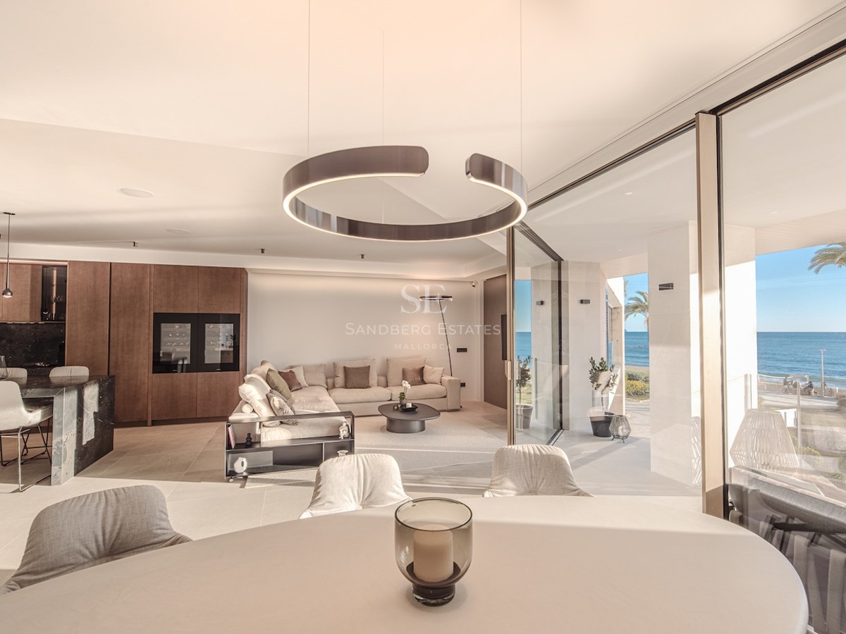 Bright open-plan living room with floor-to-ceiling glass doors opening to a terrace with sea views and palm trees.