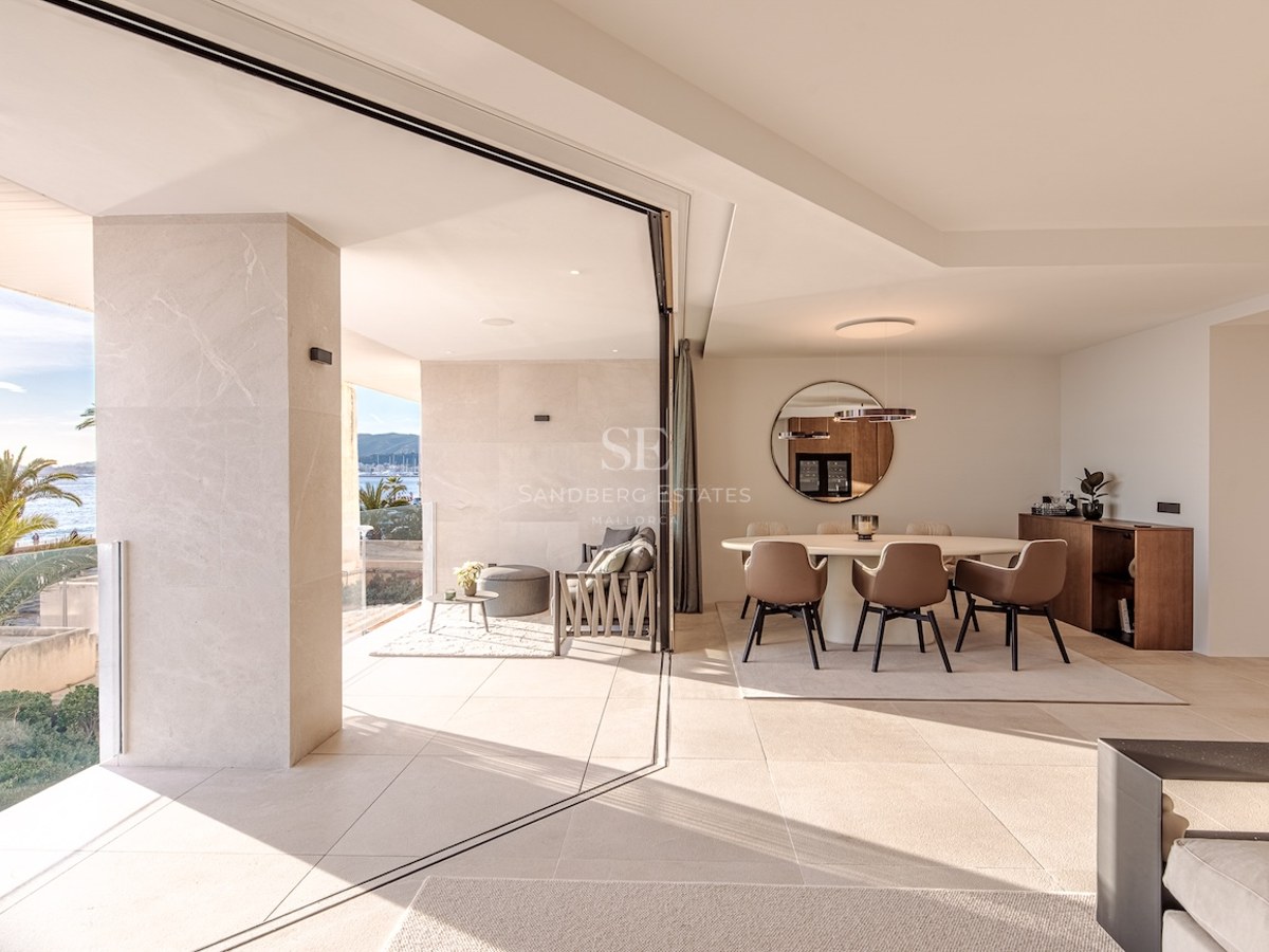 Contemporary dining room with beige stone floors and large sliding glass doors opening to a terrace with sea views.