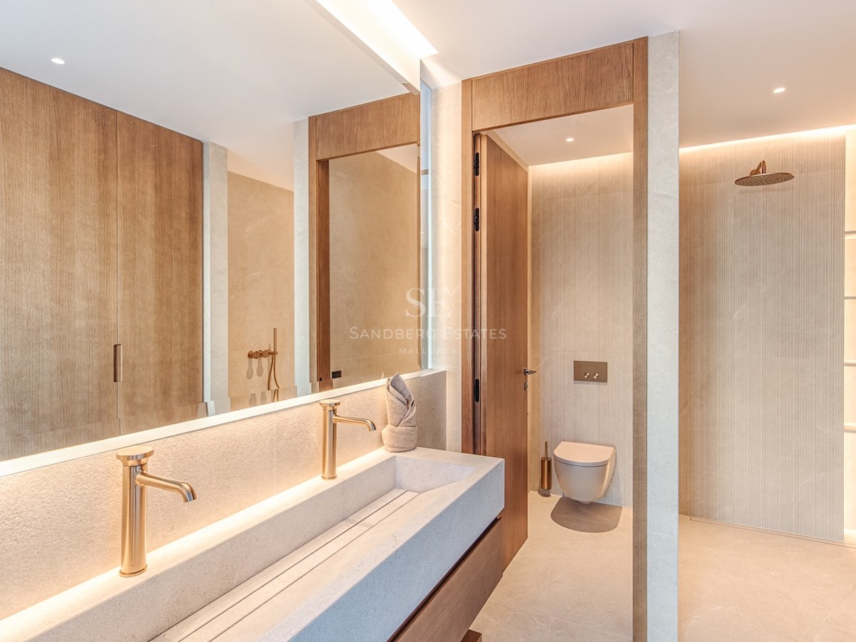 Modern bathroom featuring a long stone double sink, gold faucets, a walk-in shower, and wood paneling.