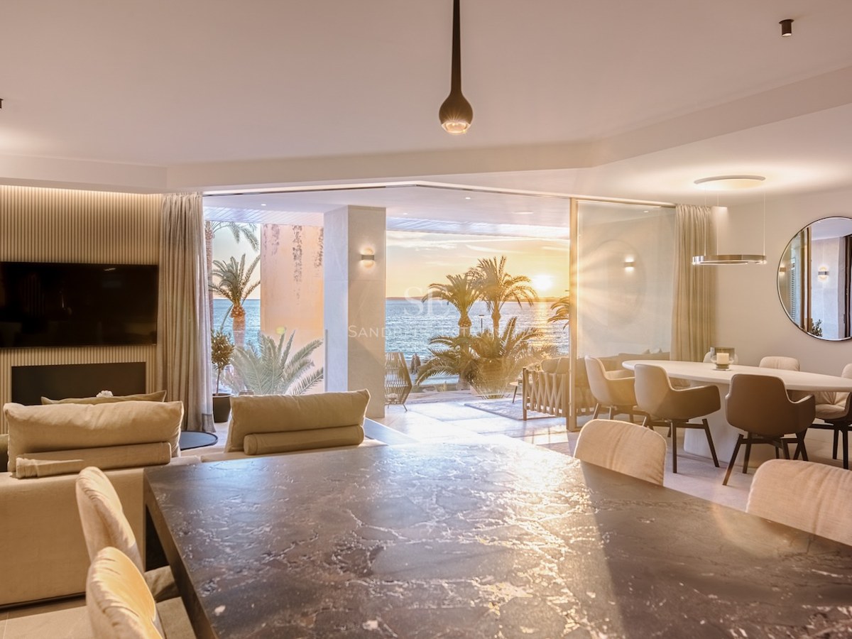 Luxury open-plan living and dining room with floor-to-ceiling glass doors opening onto a terrace with sea views at sunset.