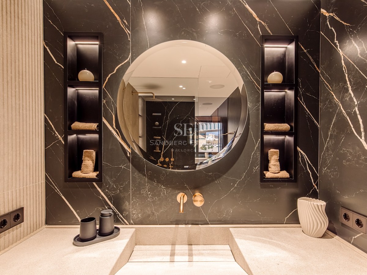 Modern bathroom vanity featuring a round mirror, black marble wall with gold veins, and integrated stone sink.