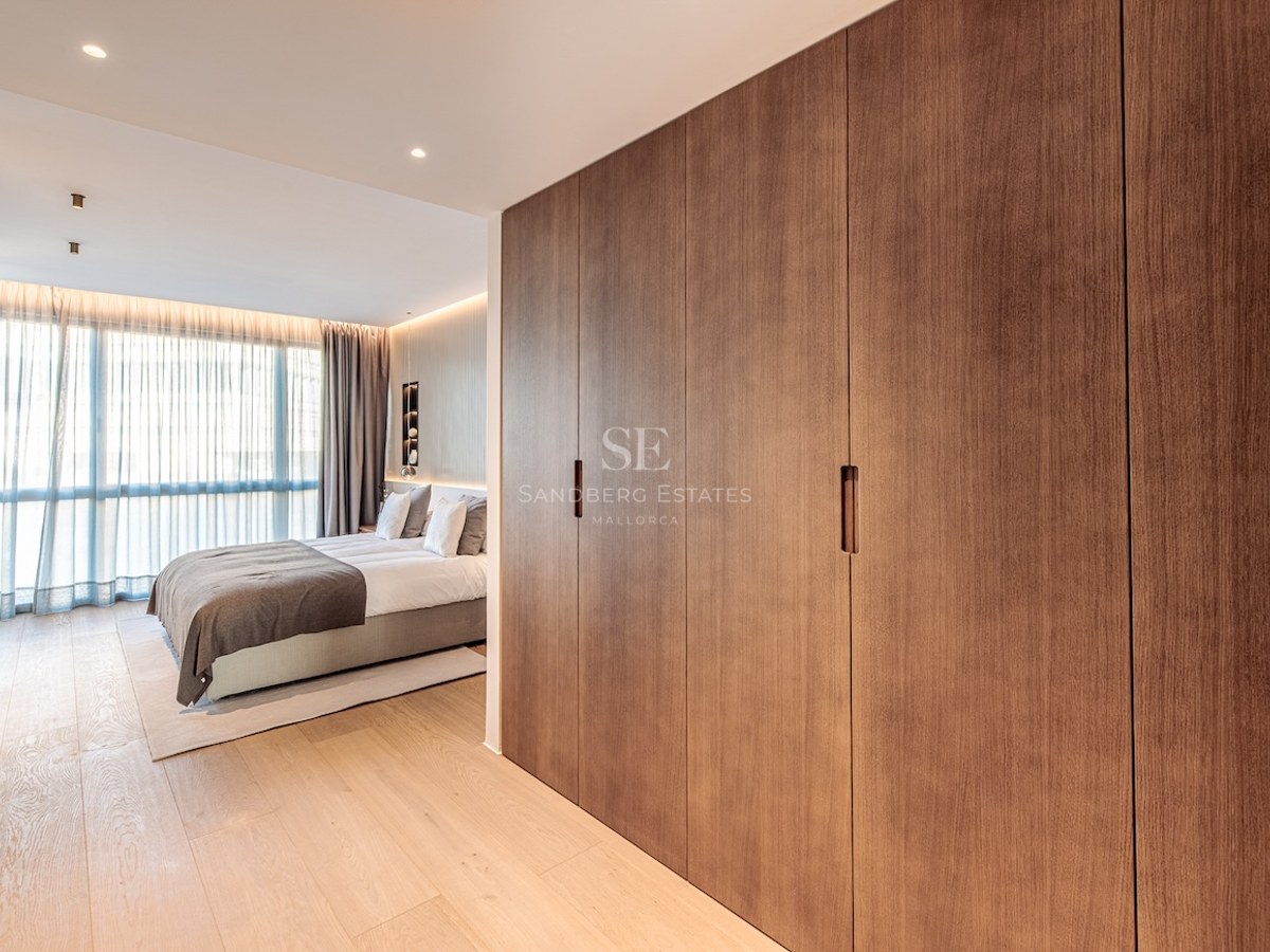 Modern bedroom featuring floor-to-ceiling wood wardrobes, light oak flooring, and large windows with soft curtains.