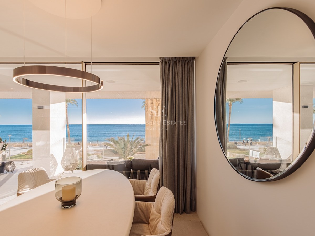 Luxury dining room featuring a white oval table and floor-to-ceiling windows overlooking the Mediterranean beach.