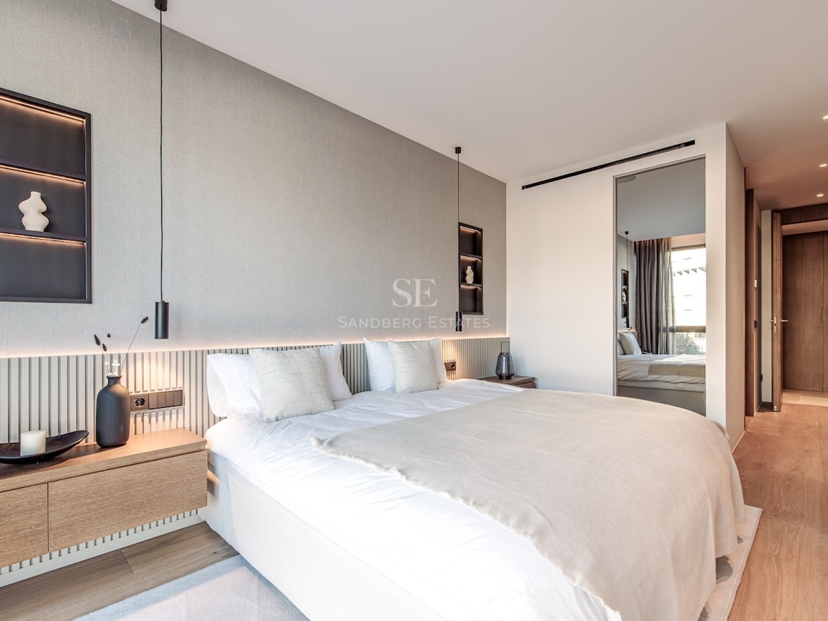 Modern master bedroom featuring a large bed, slatted wood headboard, integrated LED lighting, and neutral decor.
