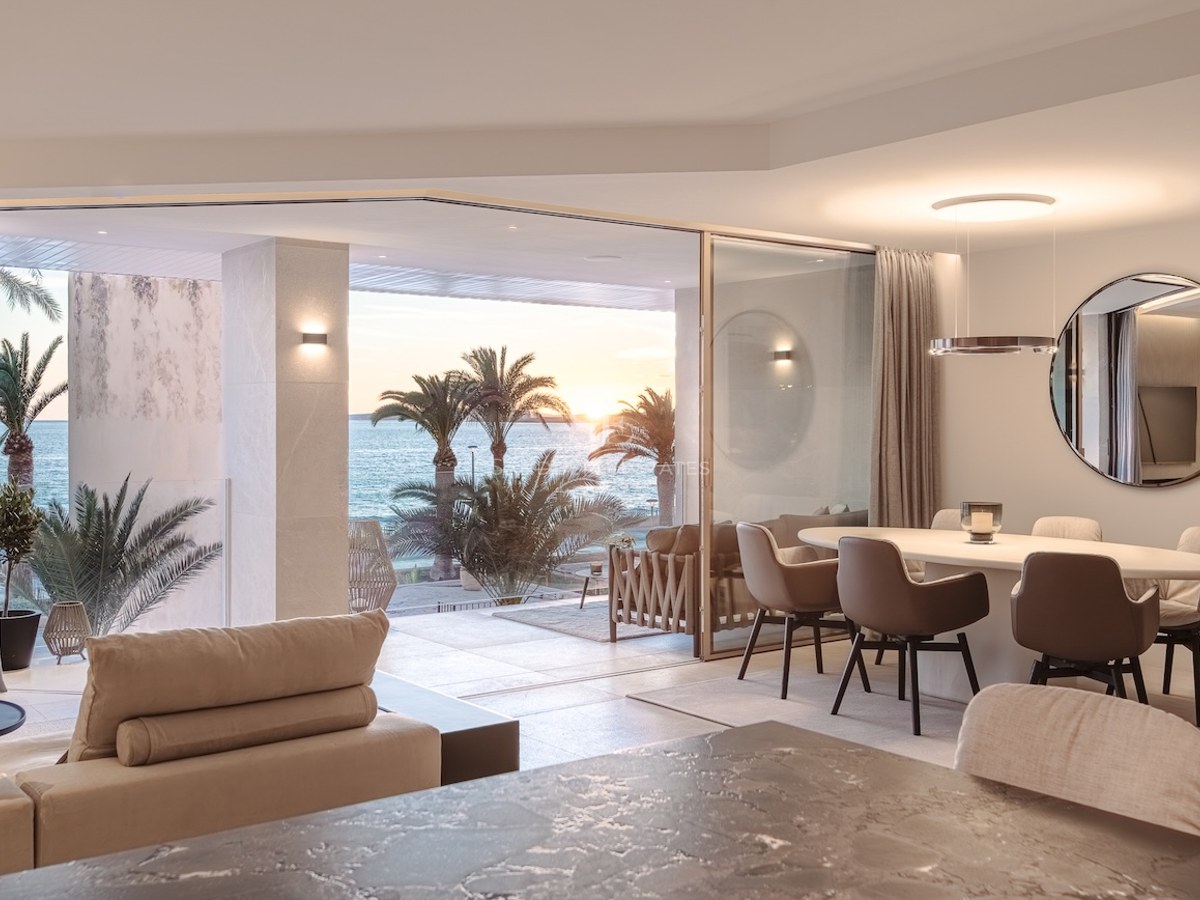 Contemporary dining room with marble table opening onto a terrace with palm trees and sunset sea views.