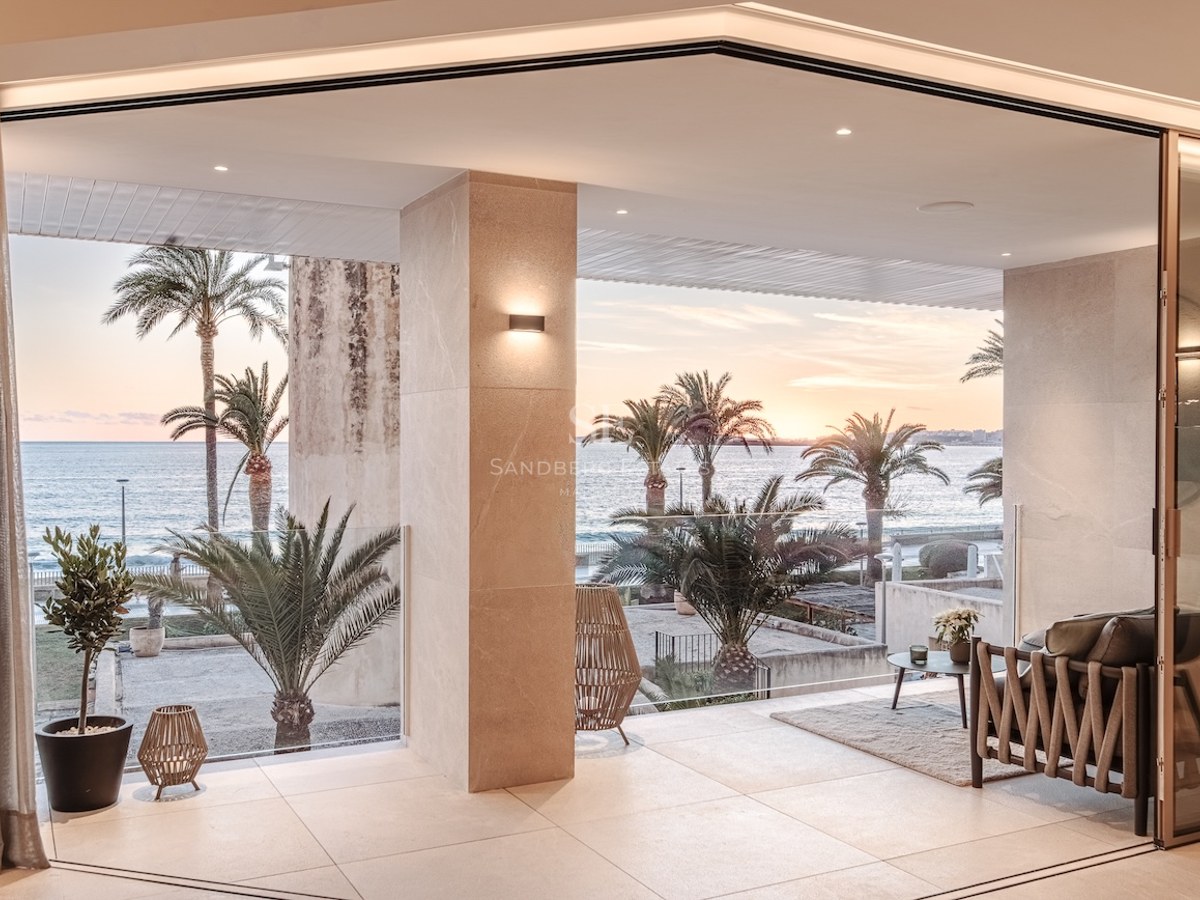 Modern terrace with stone flooring and glass railings overlooking the sea and palm trees at sunset.