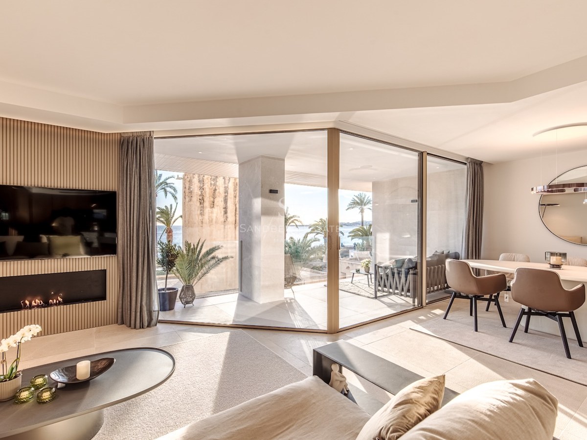 Modern living and dining room with glass doors opening to a terrace with sea views and a slatted wood fireplace wall.