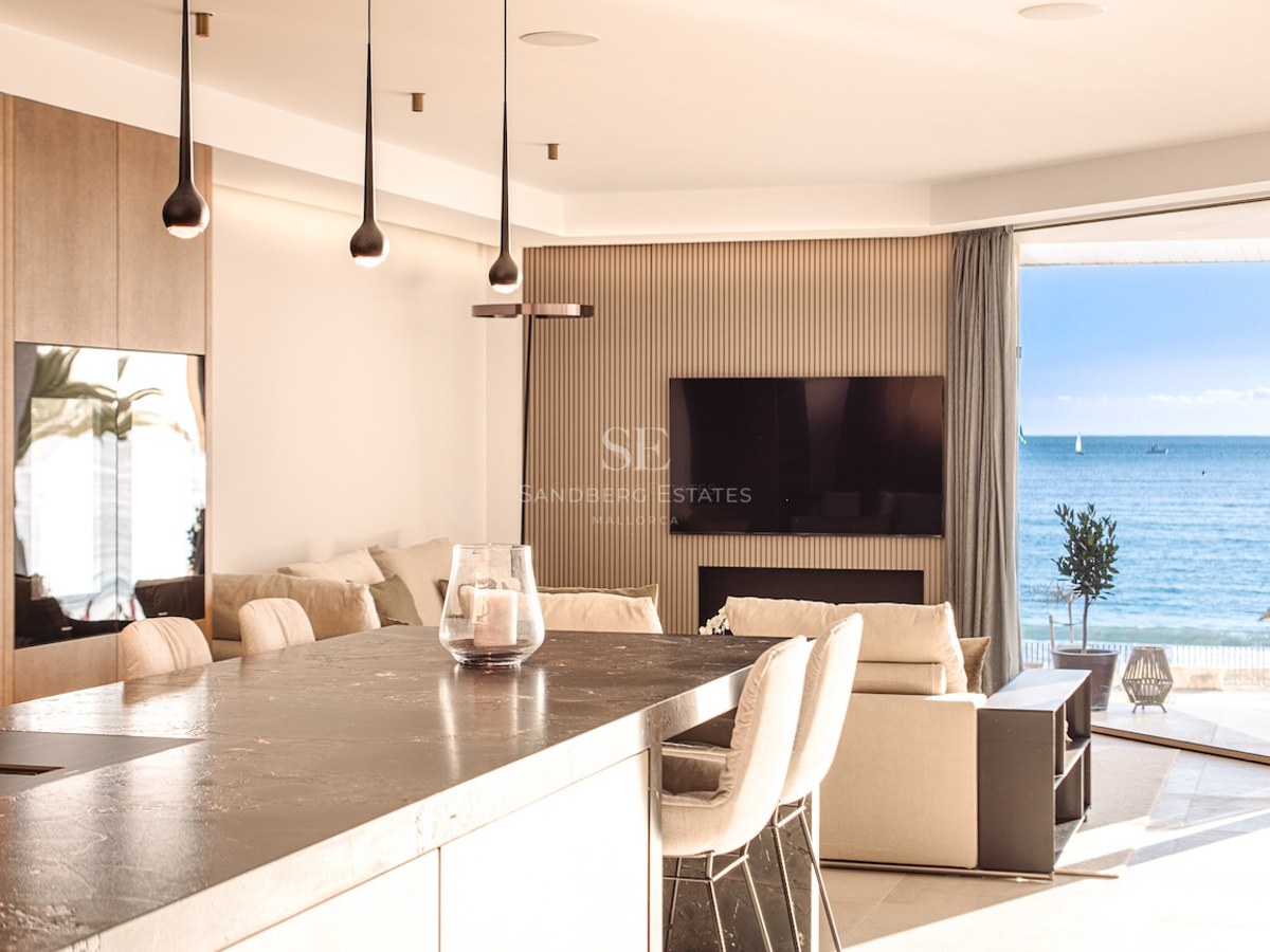 Luxury open-plan living room and kitchen featuring a dark stone island and floor-to-ceiling windows overlooking the sea.