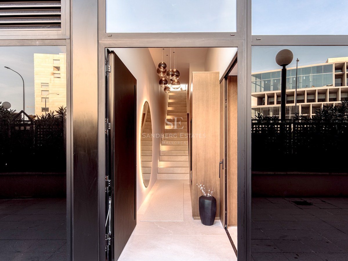 View through an open black door into a modern hallway featuring a stone staircase and designer glass pendant lights.