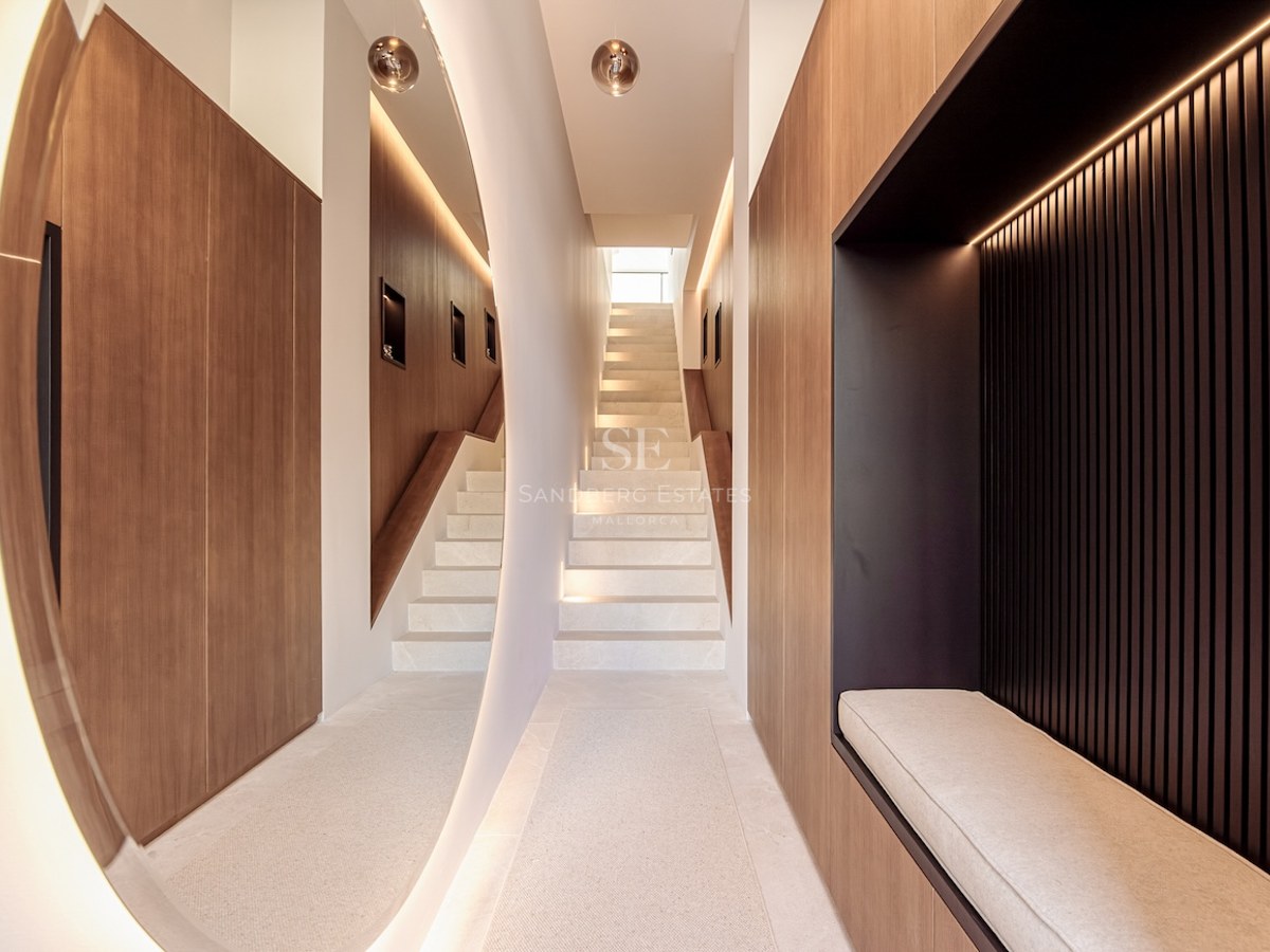 Modern hallway with floating stone staircase, wood paneling, large backlit circular mirror, and built-in seating niche.