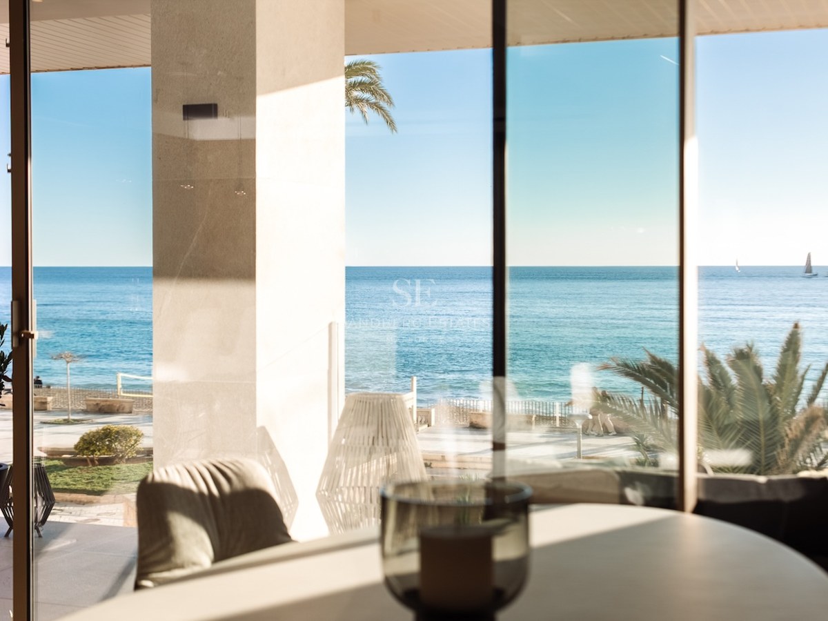 Mediterranean Sea view through floor-to-ceiling glass doors from a modern interior with a covered terrace.