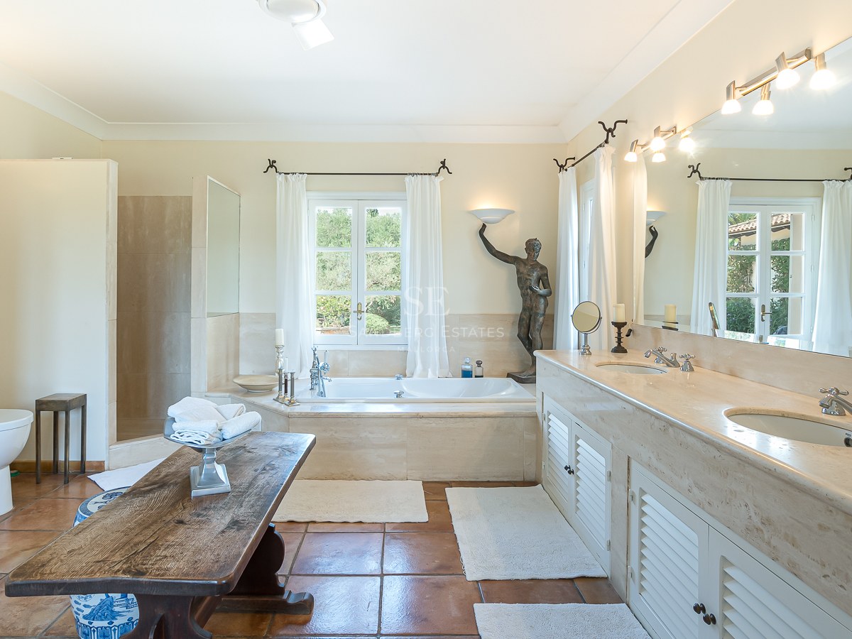 Großes Badezimmer mit Doppelwaschtisch aus Marmor, Einbaubadewanne am Fenster und Terrakottaboden.