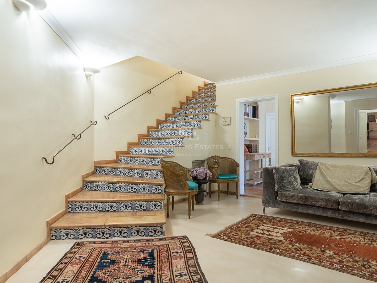 Innenansicht einer Eingangshalle mit einer Treppe mit blau-weißen Fliesen, Samtsofa und Orientteppichen.