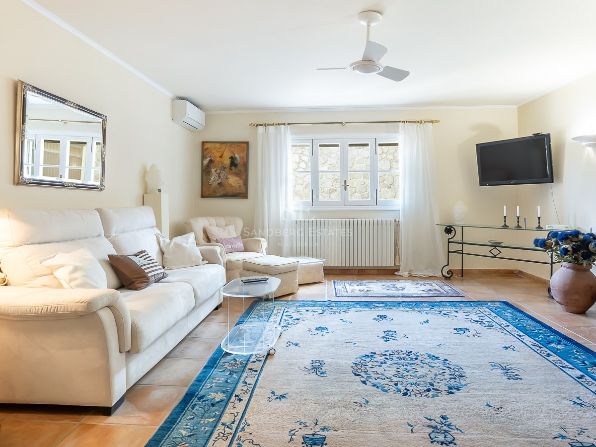 Helles Wohnzimmer mit weißem Sofa, großem blauem Teppich, Terrakottaboden und Deckenventilator.