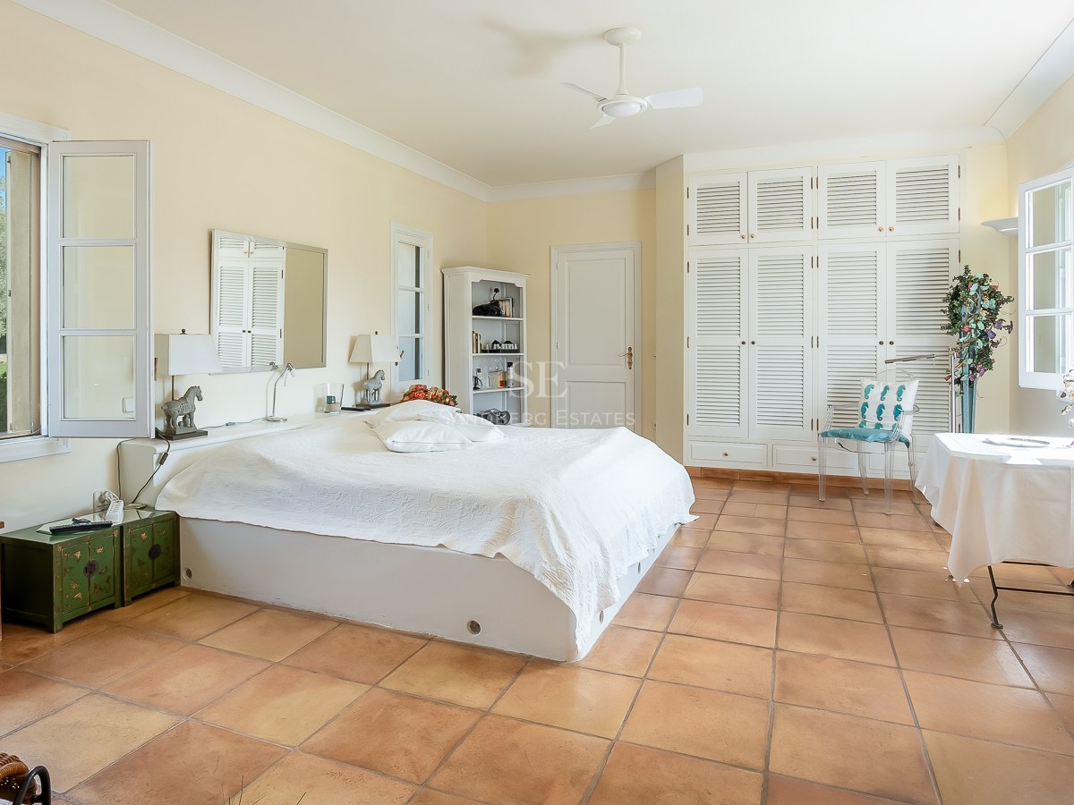 Geräumiges Schlafzimmer mit Terrakottaboden, weißen Lamellenschränken und Fenstern mit Blick auf einen grünen Garten.