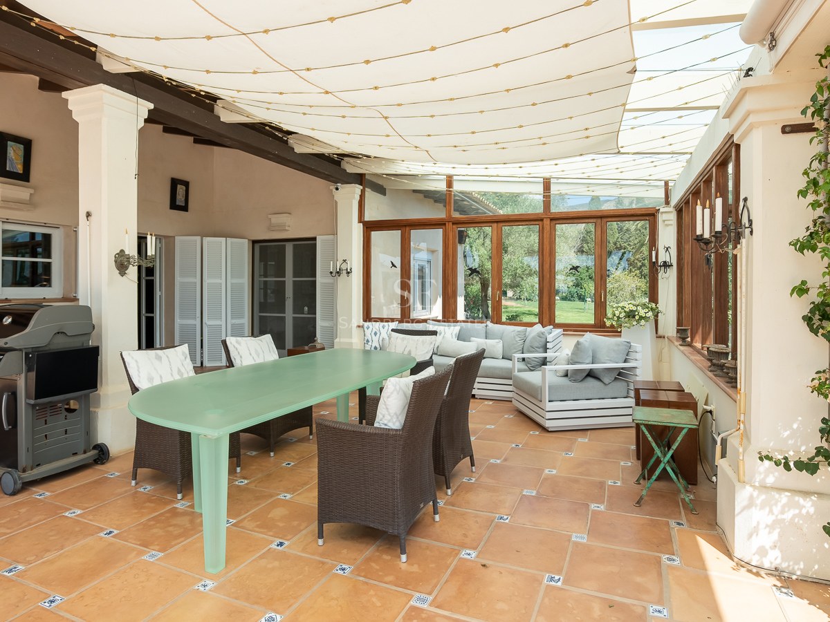 Überdachte Terrasse mit Terrakottafliesen, Esstisch, Loungebereich und Grill unter einer Markise.
