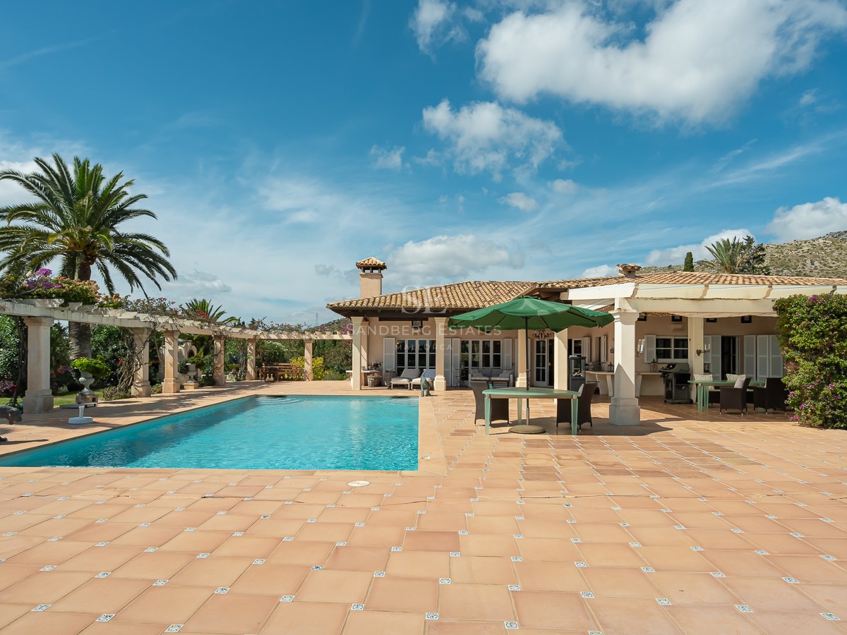 Großer rechteckiger Pool, umgeben von einer Terrakotta-Terrasse und einer weißen Villa unter blauem Himmel.