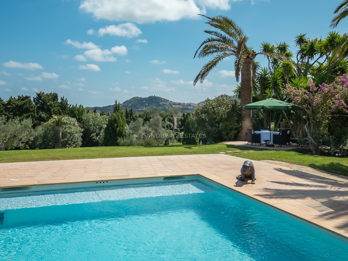 Piscine rectangulaire avec terrasse en terre cuite entourée d'une pelouse, de palmiers et de vues sur les collines.