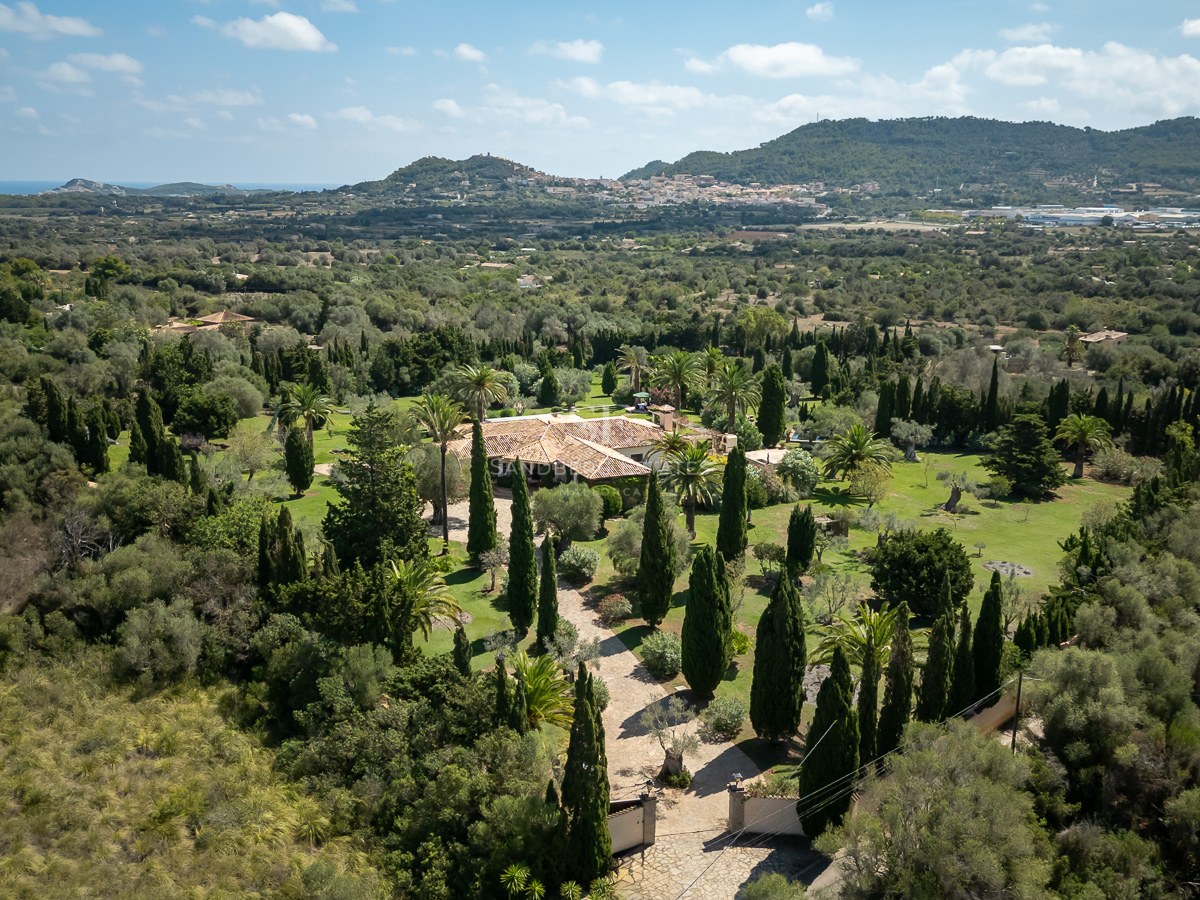 Vue aérienne d'une villa de luxe avec toit en terre cuite entourée de jardins verdoyants et de montagnes à Majorque.
