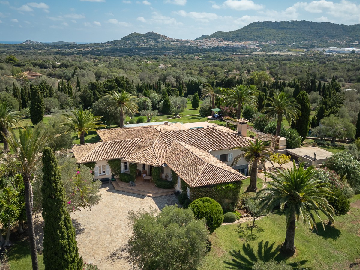 Luftaufnahme einer herrschaftlichen mediterranen Villa mit Terrakotta-Dächern inmitten einer üppigen Parkanlage.