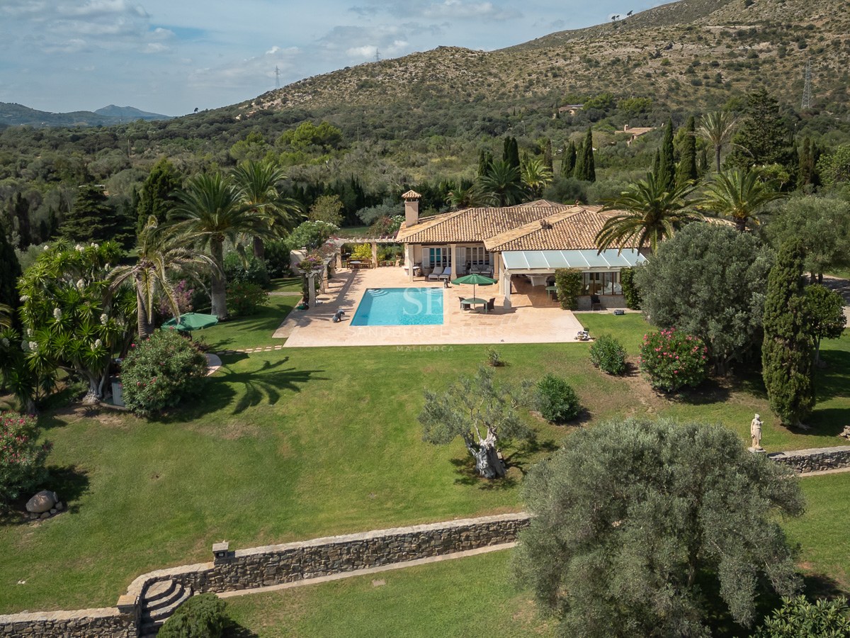 Vue aérienne d'une villa avec toit en terre cuite, piscine, grand jardin et montagnes en arrière-plan.