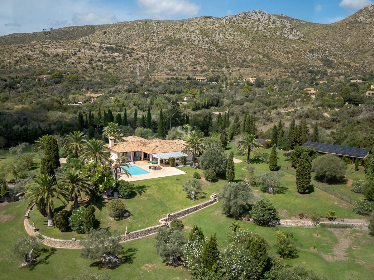 Vue aérienne d'une villa méditerranéenne avec piscine, grands jardins et montagnes en arrière-plan.