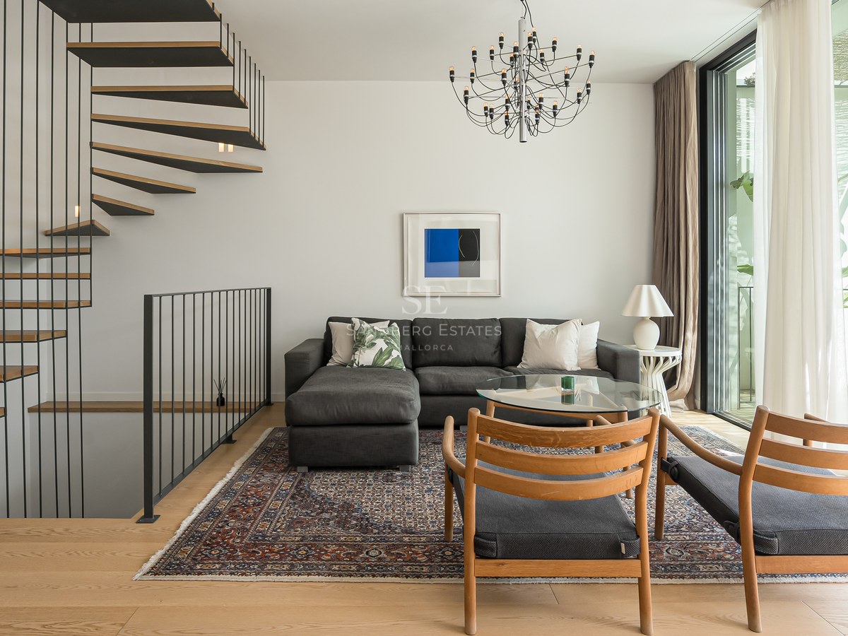Salon contemporain avec canapé gris, escalier en colimaçon en bois et grandes baies vitrées.