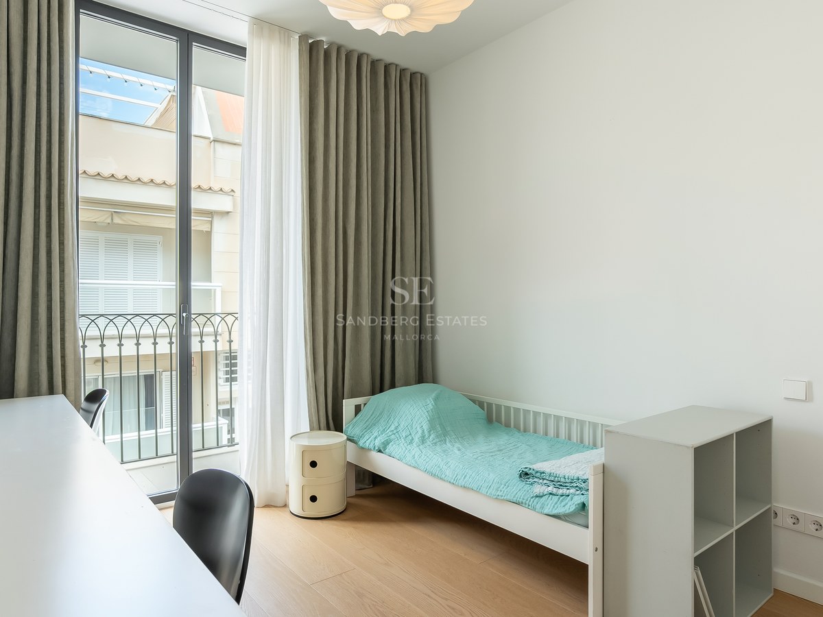 Chambre minimaliste avec un lit simple, un bureau blanc, de grandes portes vitrées et un parquet en bois clair.