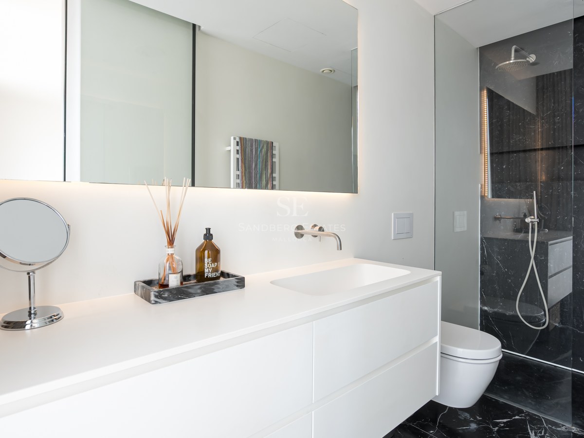 Salle de bain minimaliste blanche avec meuble vasque suspendu et douche à l'italienne en marbre noir.
