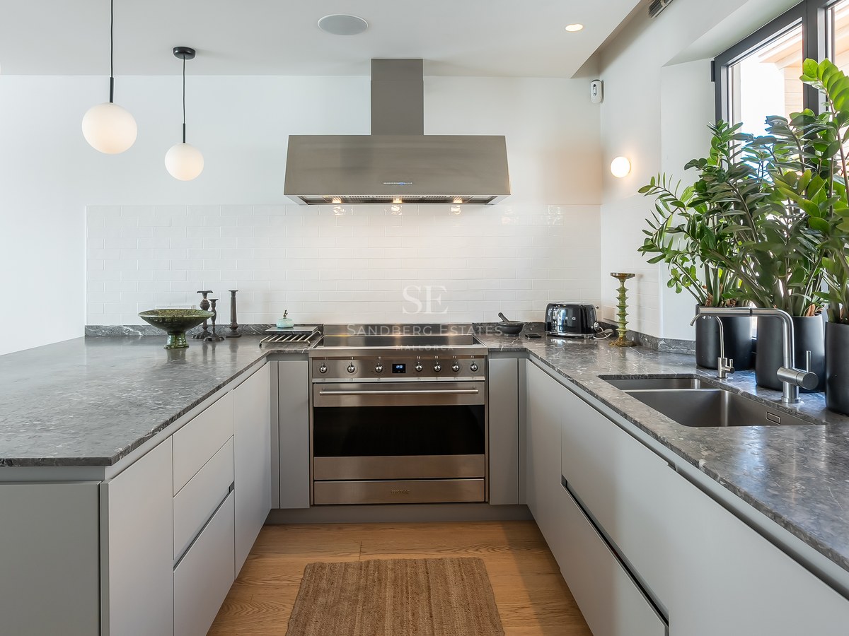 Cuisine moderne en U avec plans de travail en pierre grise, appareils en inox et lumière naturelle.