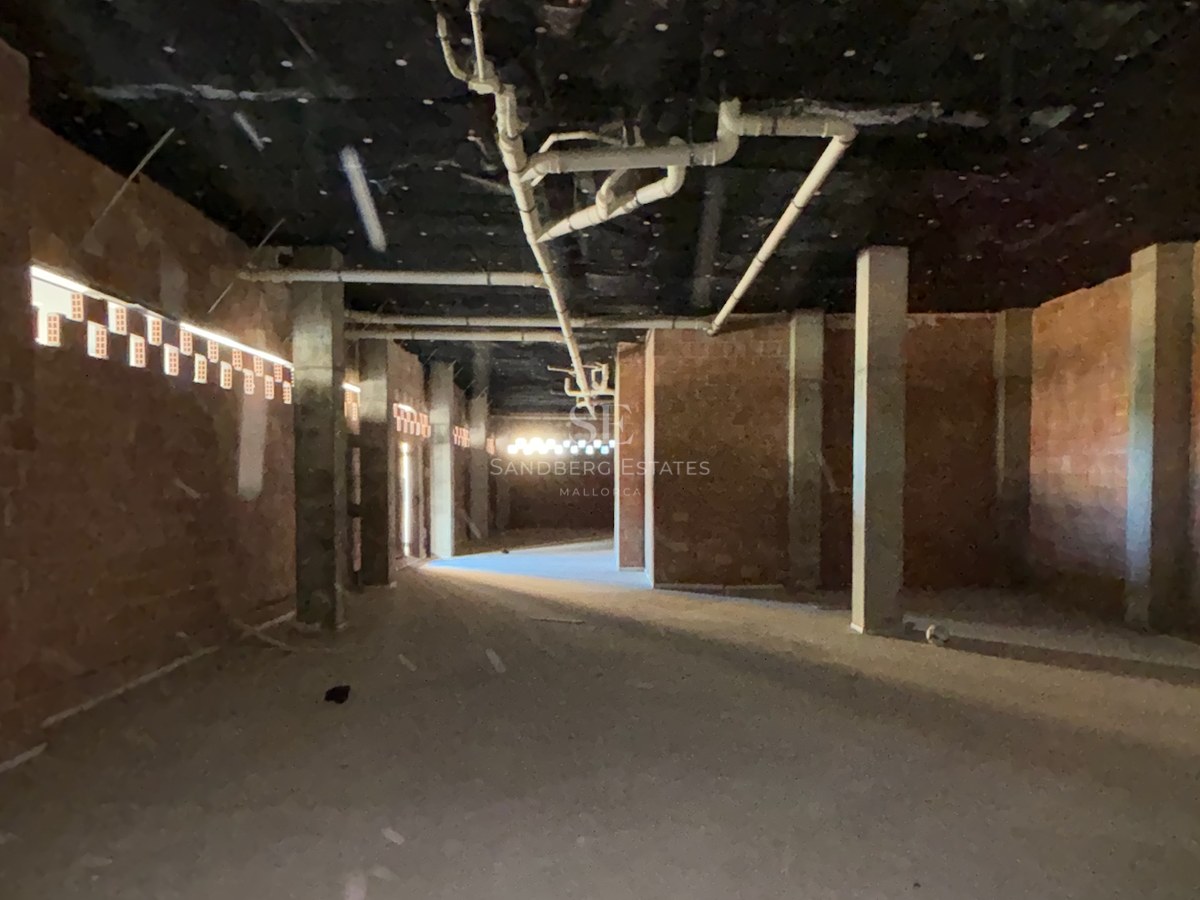 Raw interior space under construction with exposed brick walls, concrete pillars, and ceiling piping.