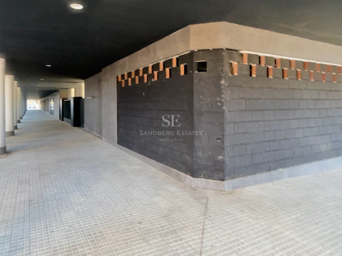 A long, covered outdoor walkway with dark brick walls, white columns, and grey paved flooring.