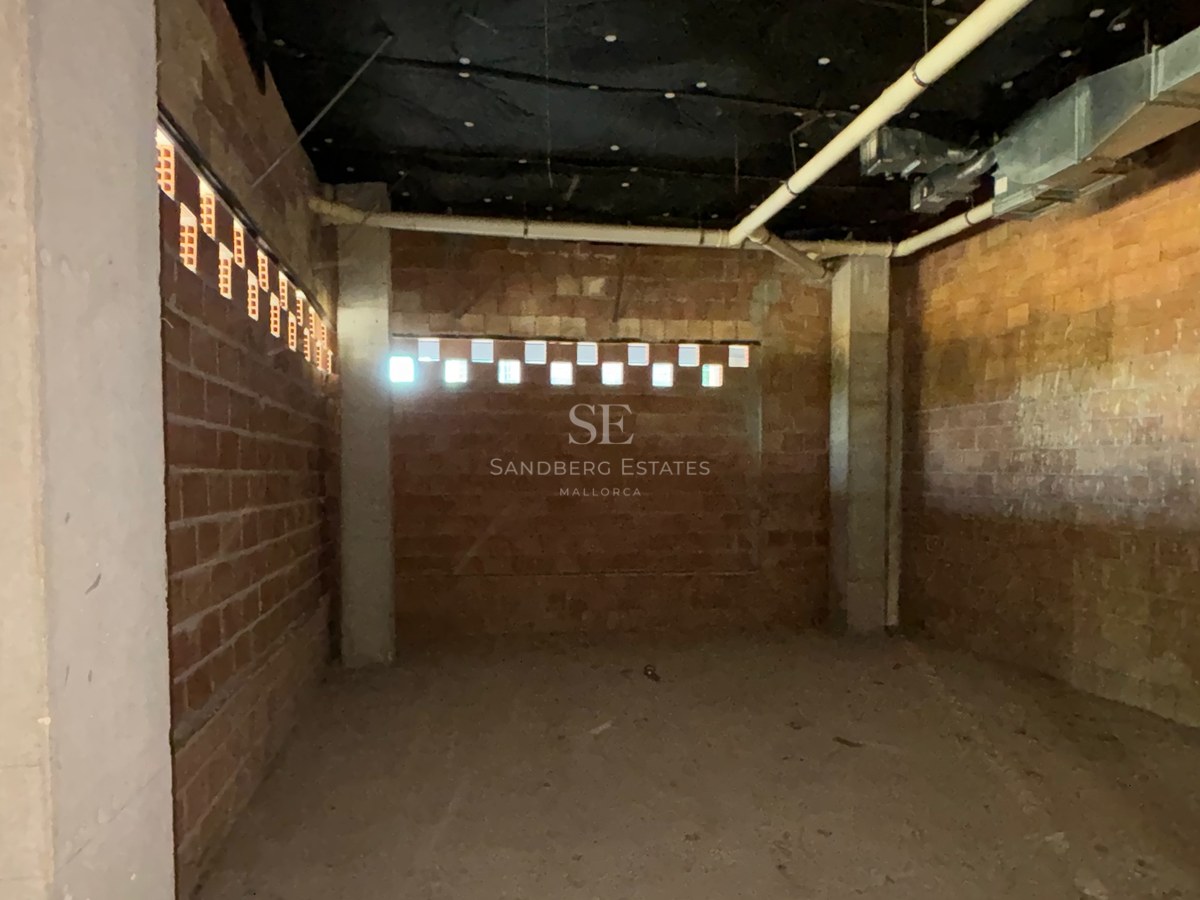Unfinished basement room with red brick walls, concrete pillars, and exposed utility pipes.