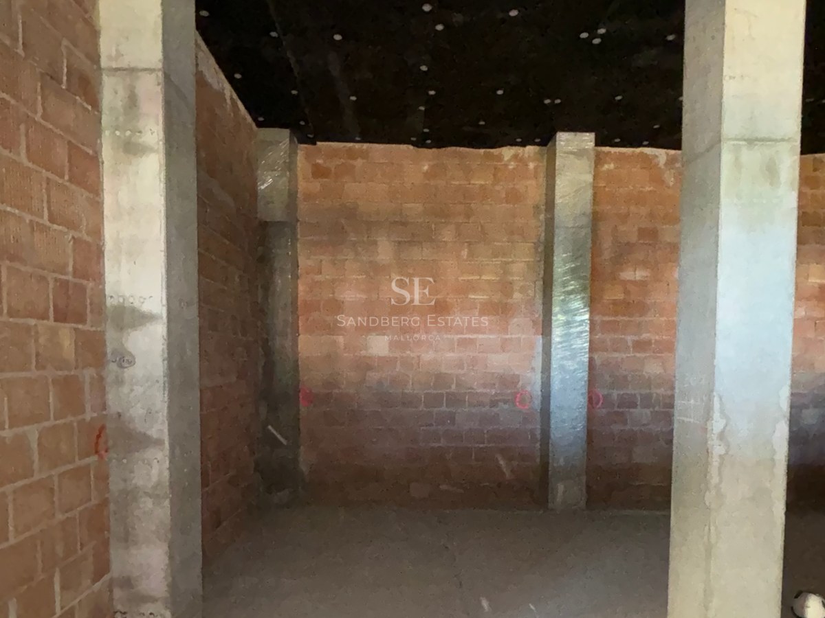 Interior view of a construction site featuring raw brick walls, concrete pillars, and an insulated ceiling.