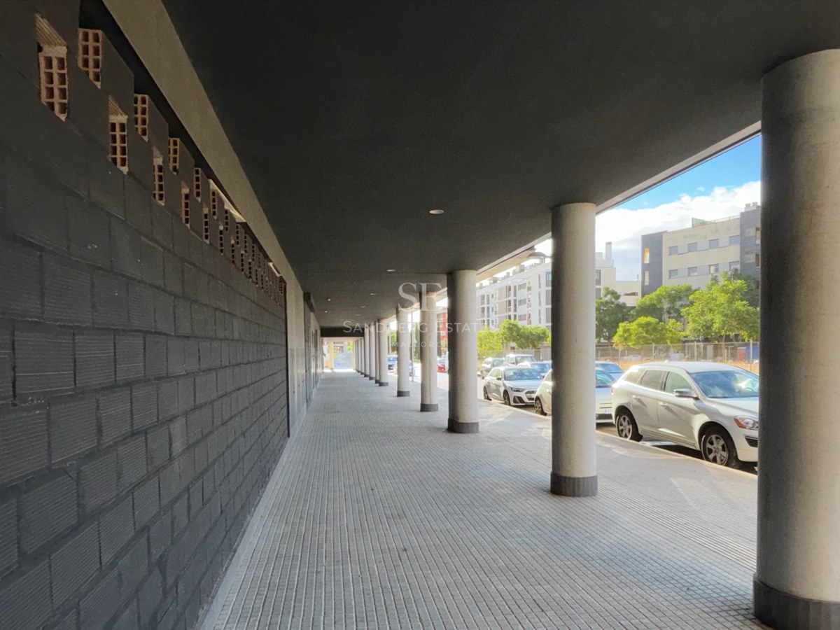Covered walkway featuring concrete pillars and a dark grey brick wall in an urban setting.
