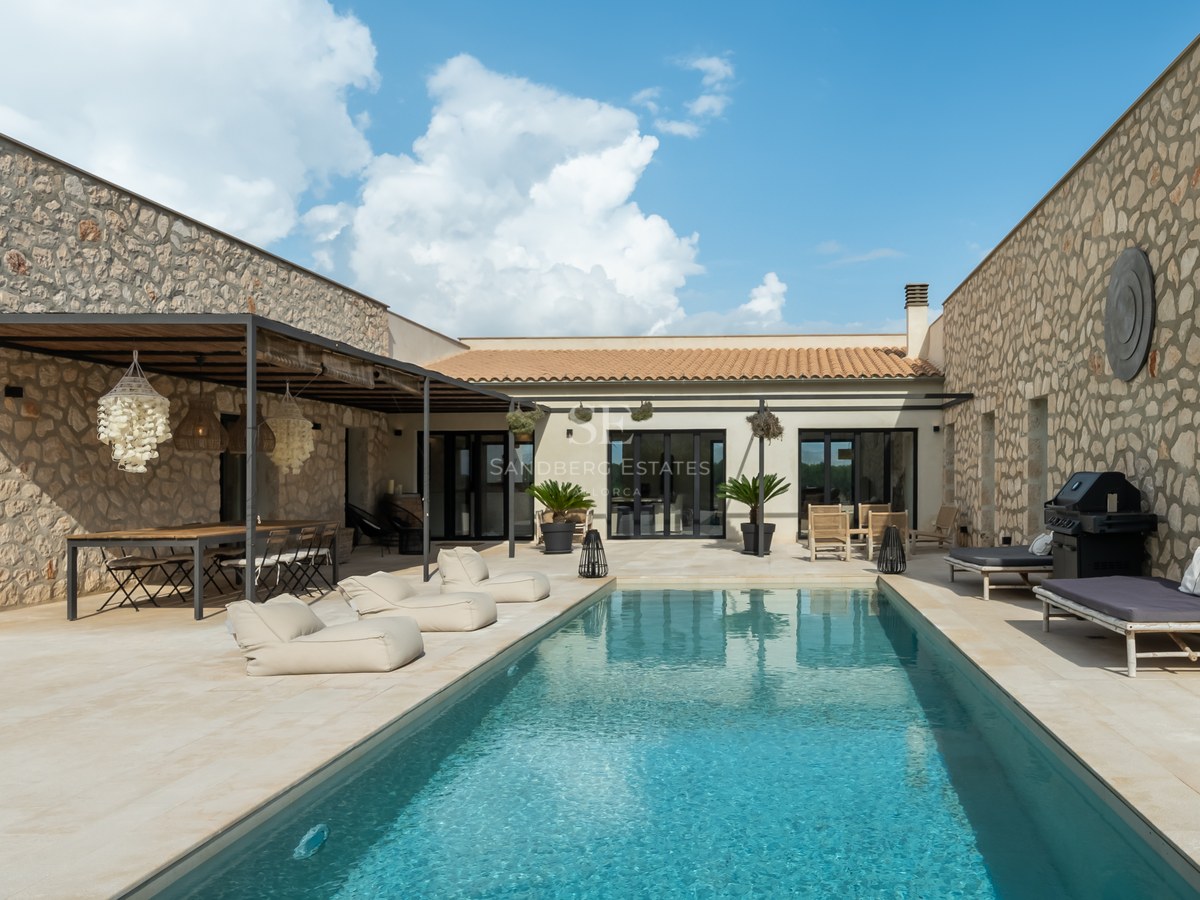 Cour centrale d'une villa de luxe en pierre avec piscine rectangulaire et espace repas ombragé.