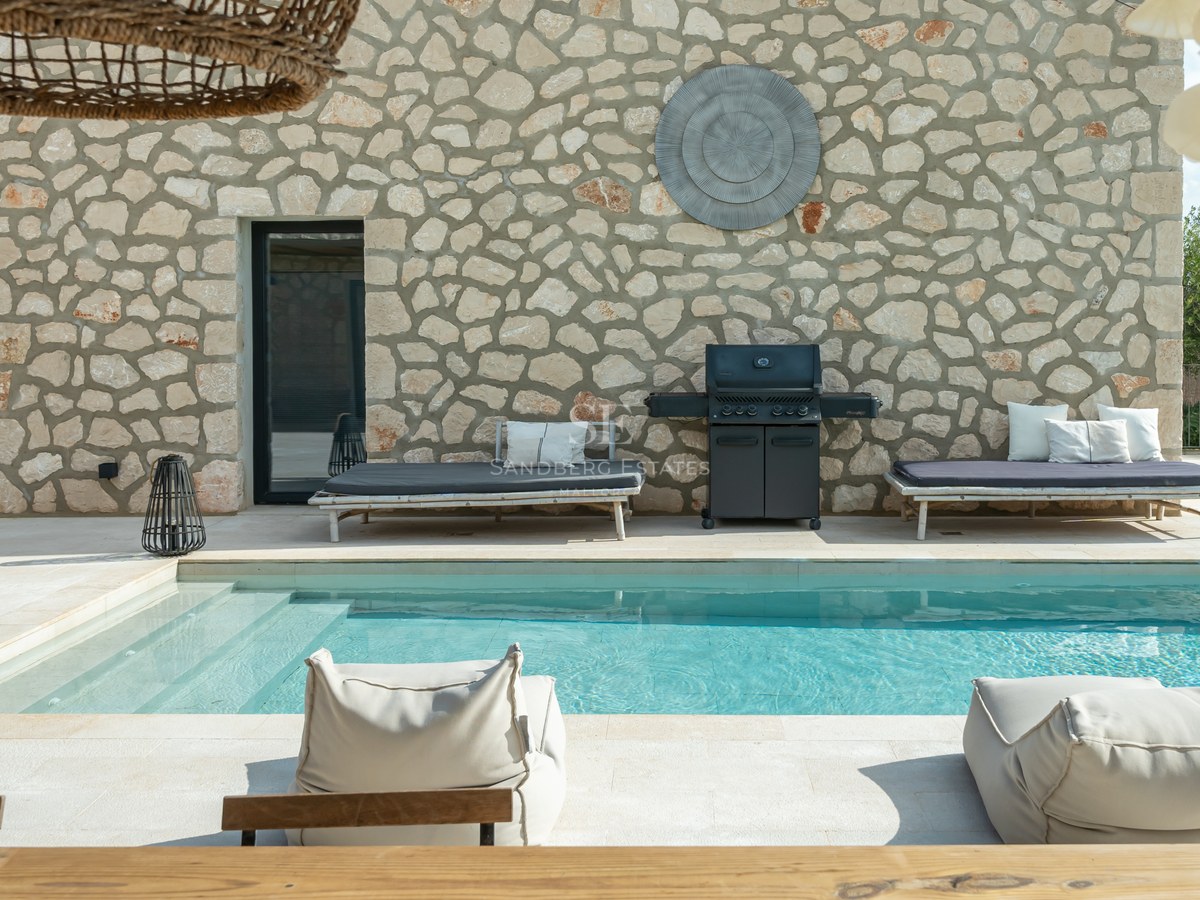 Piscine de luxe avec mur en pierre naturelle, barbecue intégré et mobilier de détente moderne.