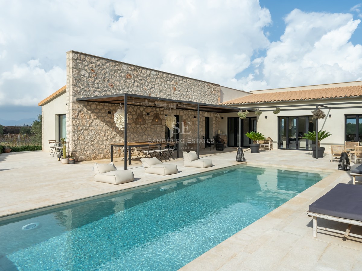 Piscine de luxe à côté d'une façade en pierre naturelle avec coin repas sous pergola et bains de soleil.